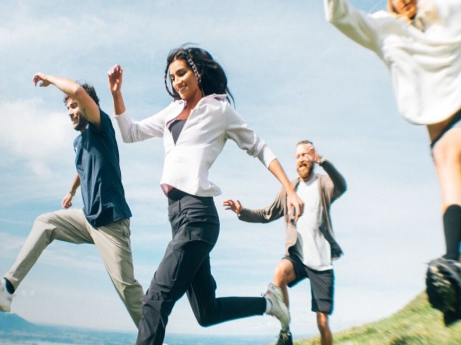 Four people in summer hiking gear run across a field
