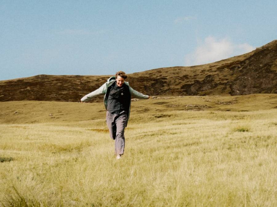 Man in summer hiking clothes running across a field with outstretched arms